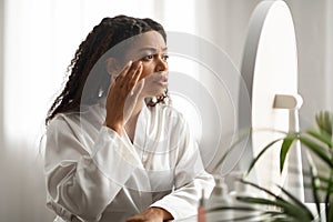 Aging Signs. Stressed Black Woman Touching Face Skin And Looking At Mirror