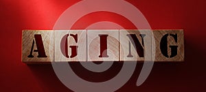 Aging - word from wooden blocks with letters, on red background. Growing old senescence aging healthcare concept photo
