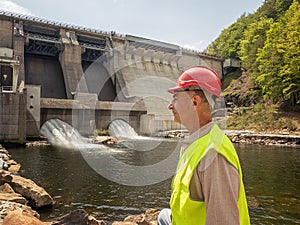 An aging worker in a helmet against the backdrop of hydroelectric turbines