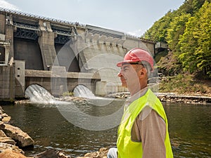 An aging worker in a helmet against the backdrop of hydroelectric turbines