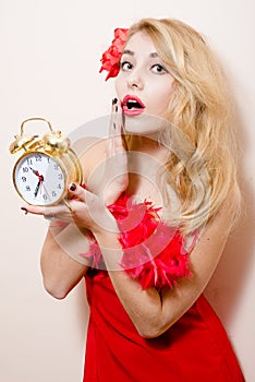 Agitated beautiful funny young blond pinup pretty woman with alarm-clock in red dress wonderingly looking at camera