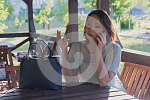 Agitated woman is talking on a smartphone in the gazebo of a street cafe