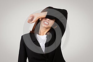 Agitated young businesswoman in a black blazer covering her eyes with her arm