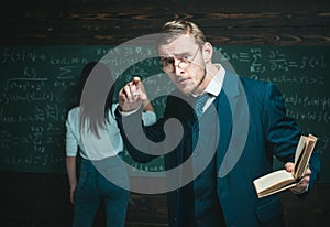 Agitated young professor passionately explaining mathematic formula. Handsome teacher holding a book while giving a