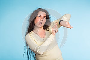 Agitated young woman pointing her wrist watch over blue background