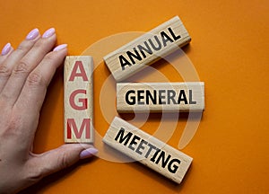 AGM - Annual general meeting symbol. Concept word AGM on wooden cubes. Businessman hand. Beautiful orange background. Business and