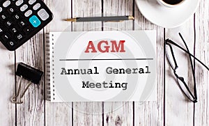 AGM Annual General Meeting is written in a white notepad near a calculator, coffee, glasses and a pen. Business concept