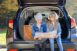 Agreeable boy and girl are looking at the road map while sitting in the auto`s trunk and discussing the move direction