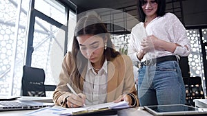 Agreeable responsible beautiful female office worker underwrite the business document which giving her female colleague