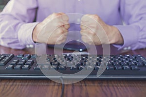 Agression in the Internet, man sitting behind keyboard with hands fists clenched photo