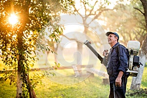 Agricultural details with farmer using sprayer machine for pesticide control in fruit orchard during sunset time