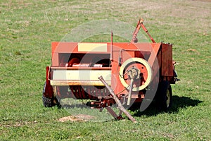 Agricultural farming haymaking equipment left in local field after heavy usage surrounded with green grass