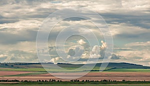 Agricultural fields on the hills in steppe under heavy clouds sky.