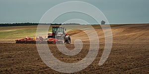 agricultural industrial landscape. a modern tractor with a trailed cultivator works on a hilly field before the autumn sowing