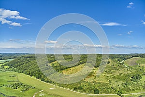 An agricultural landscape with green pasture and hill in summer. Aerial view of a farm with lush grass against a cloudy