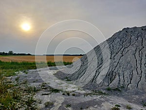 Agricultural landscape with grey heap of cement or gravel, looking like a volcano