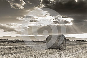 Agricultural landscape image, round hay bales on field, vibrant clouds with divine lights at sunset