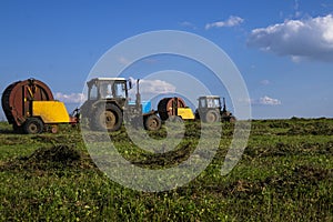 Agricultural machinery, a tractor collecting grass in a field against a blue sky. Hay harvesting, grass harvesting. Season