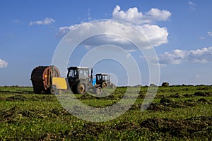 Agricultural machinery, a tractor collecting grass in a field against a blue sky. Hay harvesting, grass harvesting. Season