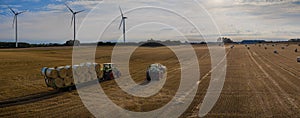 Agricultural panorama scene tractors collecting straw bales in field and loading on tractor trailer.