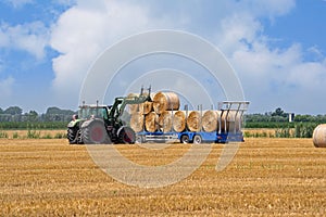 Agricultural scene, tractor loads the bales of hay on the trailer.