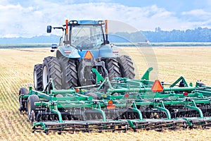 An agricultural tractor with a hitch, a harrow, stands against the background of a harvested wheat field