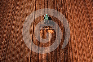 Agricultural tractor with tiller attached performing field tillage before the sowing season, aerial shot drone pov