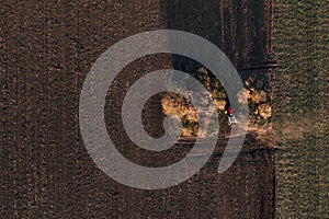 Agricultural tractor with tiller attached performing soil tillage in field, aerial view