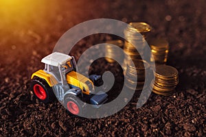 Agricultural tractor toy and golden coins on fertile soil land