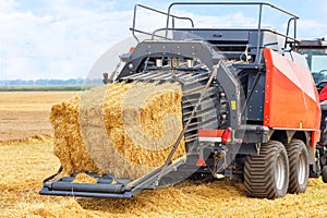 An agricultural tractor with a trailed unit turns bales of straw into dense briquettes in a wheat field