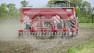 Agricultural tractor with trailer seeder working on plowed field. Rural farming