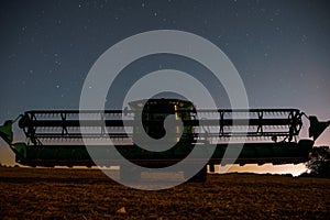 Agricultural worker utilizing a combiner in a field against a night sky illuminated by stars photo