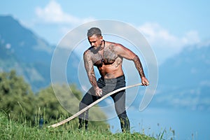 Agriculture, farmer working on alps field. Man farmer works on farm, hay making. Sexy farmer wit hay and scythe