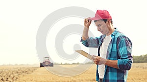 Agriculture. farmer working on a digital tablet in a field in the background a tractor plows ground in a field of wheat