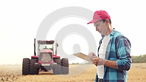 Agriculture. Farmer working on a digital tablet in a field in the background a tractor plows ground in a field of wheat