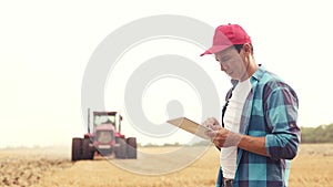 Agriculture. farmer working on a digital tablet in a field in the background a tractor plows ground in a field of wheat