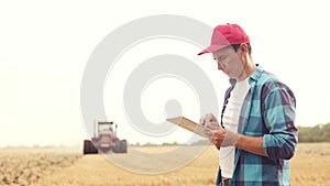 Agriculture. farmer working on a digital tablet in a field in the background a tractor plows ground in a field of wheat