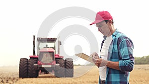 Agriculture. farmer working on a digital tablet in a field in the background a tractor plows ground in a field of wheat photo