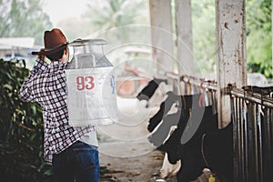 Agriculture industry, farming, people and animal husbandry concept - young man or farmer with bucket walking along cowshed