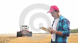 Agriculture. Portrait of a farmer working on a digital tablet in a field in the background a tractor plows ground in a