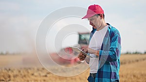 Agriculture. Portrait of a farmer working on a digital tablet in a field in the background a tractor plows the ground in