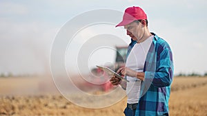 Agriculture. Portrait of a farmer working on a digital tablet in a field in the background a tractor plows the ground in