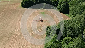 Agriculture tractor in early spring spraying farmland field with crop sprouts, aerial