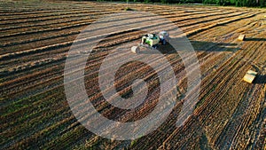 Agriculture tractor making hay bales works on the field. Aerial view of baling, baler, hay collection.