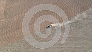 Agriculture tractor sowing crop on dusty farm field, aerial