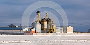 Agro silos granary elevator in winter day in snowy field. Silos on agro-processing manufacturing plant for processing drying