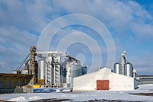 Agro silos granary elevator in winter day in snowy field. Silos on agro-processing manufacturing plant for processing drying