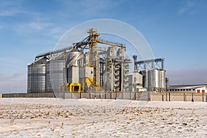 Agro silos granary elevator in winter day in snowy field. Silos on agro-processing manufacturing plant for processing drying