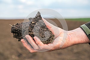 Agronomist holding a clod of earth, closeup of male hand with soil sample from agricultural field