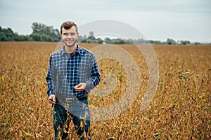 Agronomist holds tablet touch pad computer in the soy field and examining crops before harvesting. Agribusiness concept.